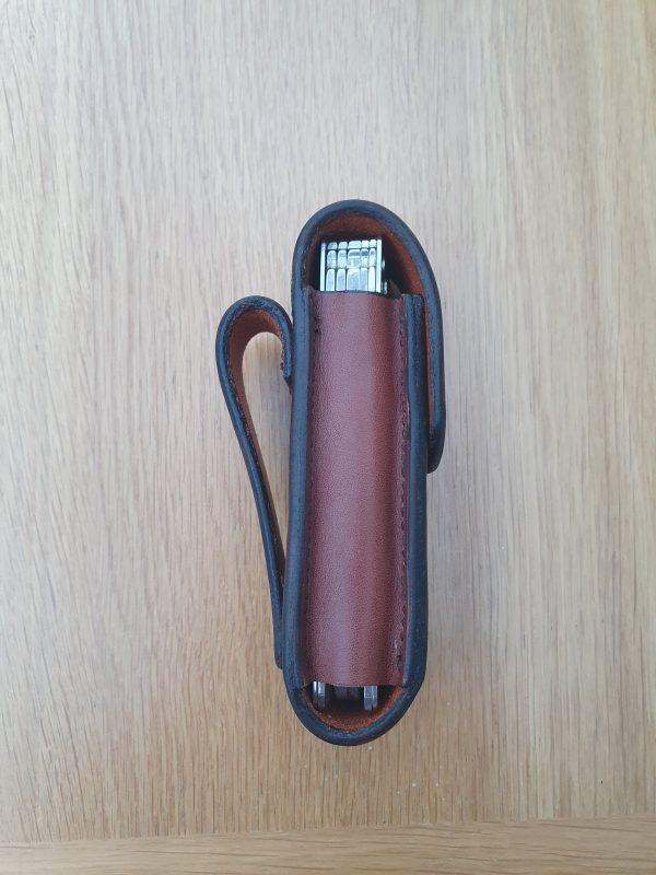 a side view of a brown leather pouch with a belt loop the pouch has black edges and there is a silver multi tool inside the pouch
